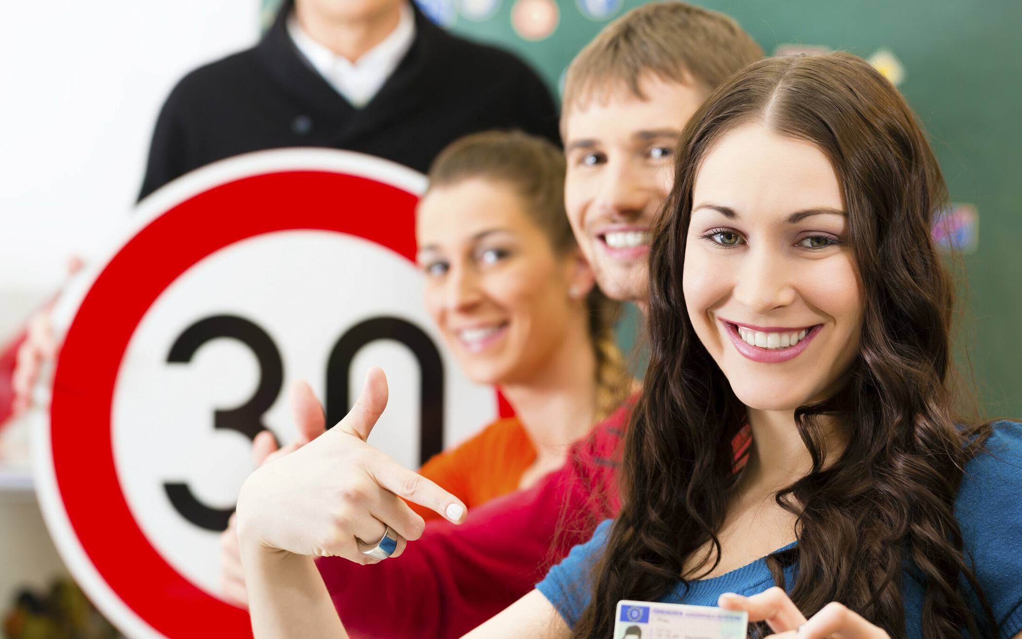  Driving school - driving instructor in his class and a female student driver looking in the Camera, in the background are traffic signs 