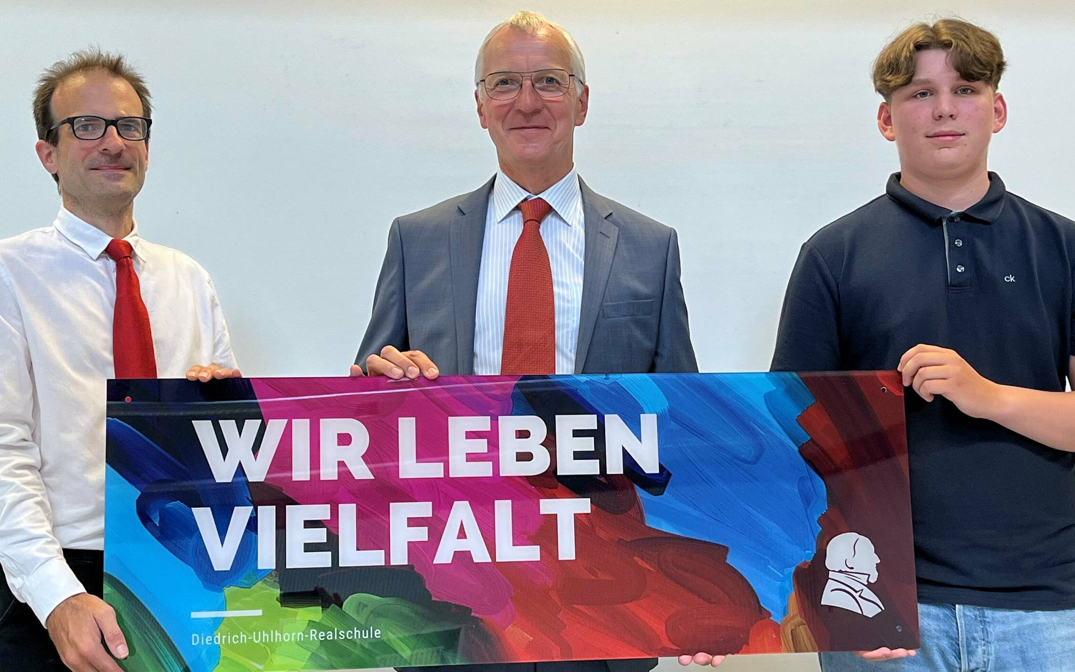  Schulpflegschaftsvorsitzender Sascha Steinert, Schulleiter Manfred Rost und Initiator Leon Coumanns präsentieren den neuen Slogan der Diedrich-Uhlhorn-Realschule. 