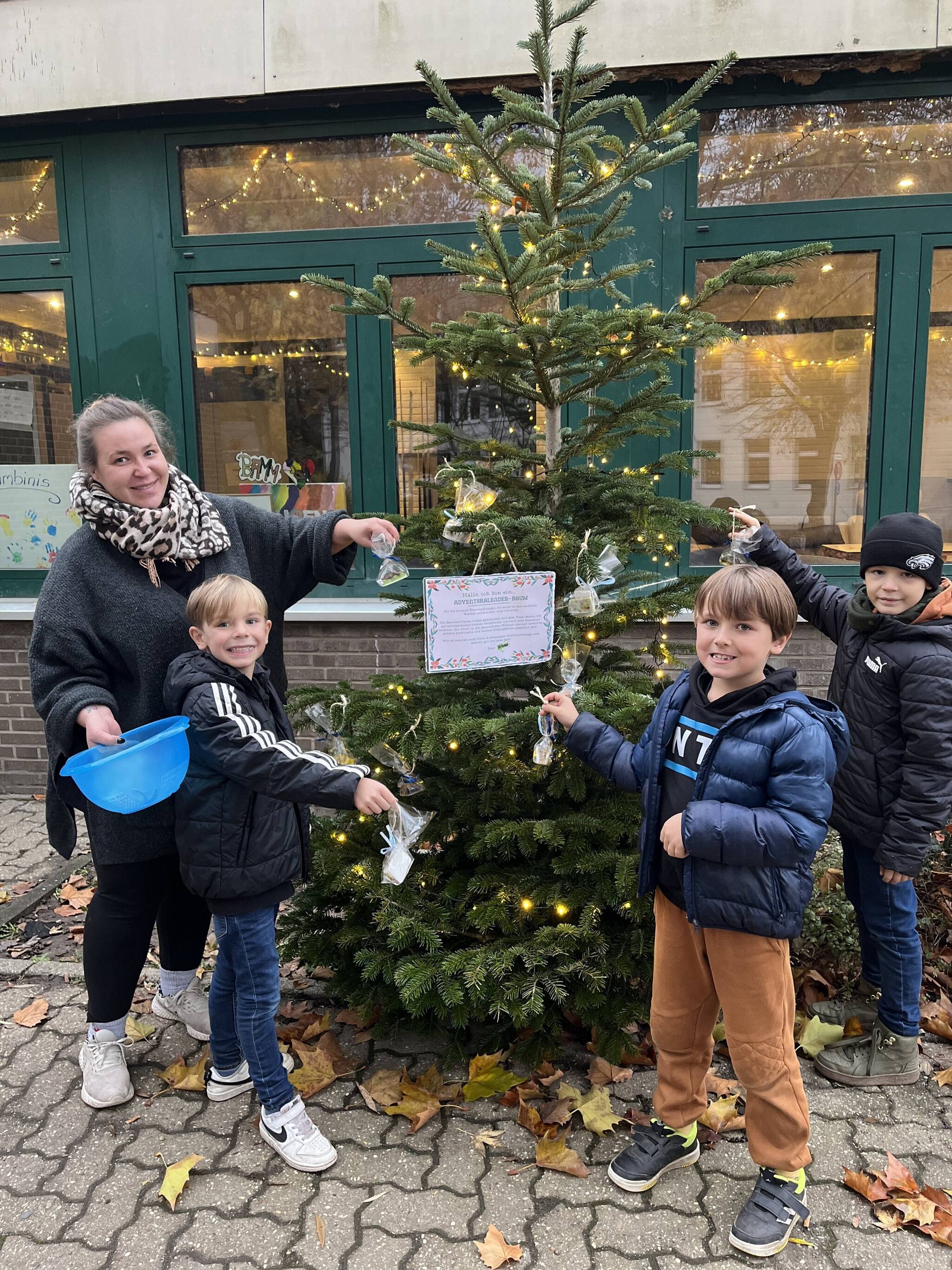  Cerise Beermann hängt mit Kindern die kleinen Aufmerksamkeiten an den Tannenbaum vor dem Jugendcafé auf.  
   