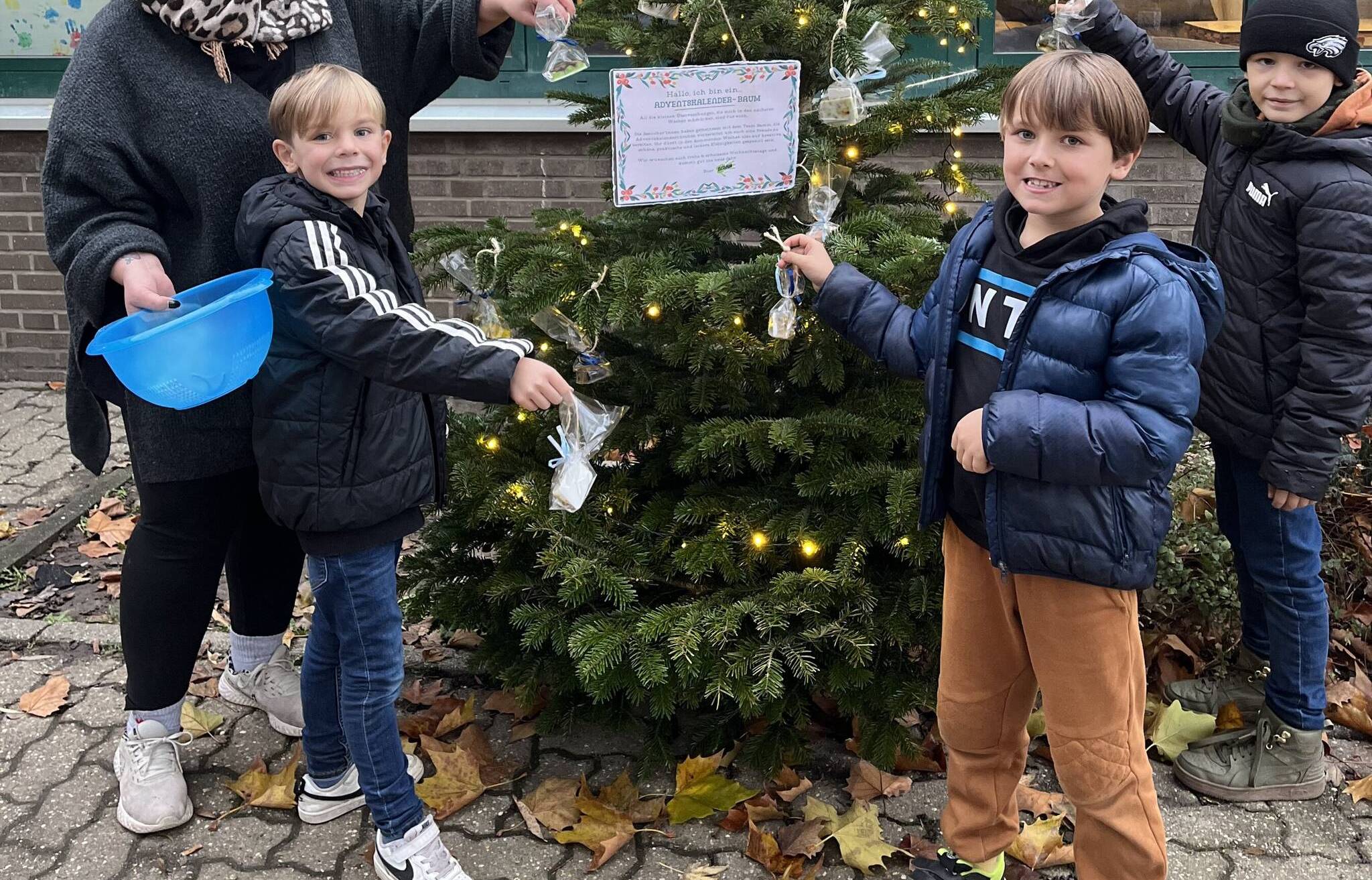  Cerise Beermann hängt mit Kindern die kleinen Aufmerksamkeiten an den Tannenbaum vor dem Jugendcafé auf.  
   