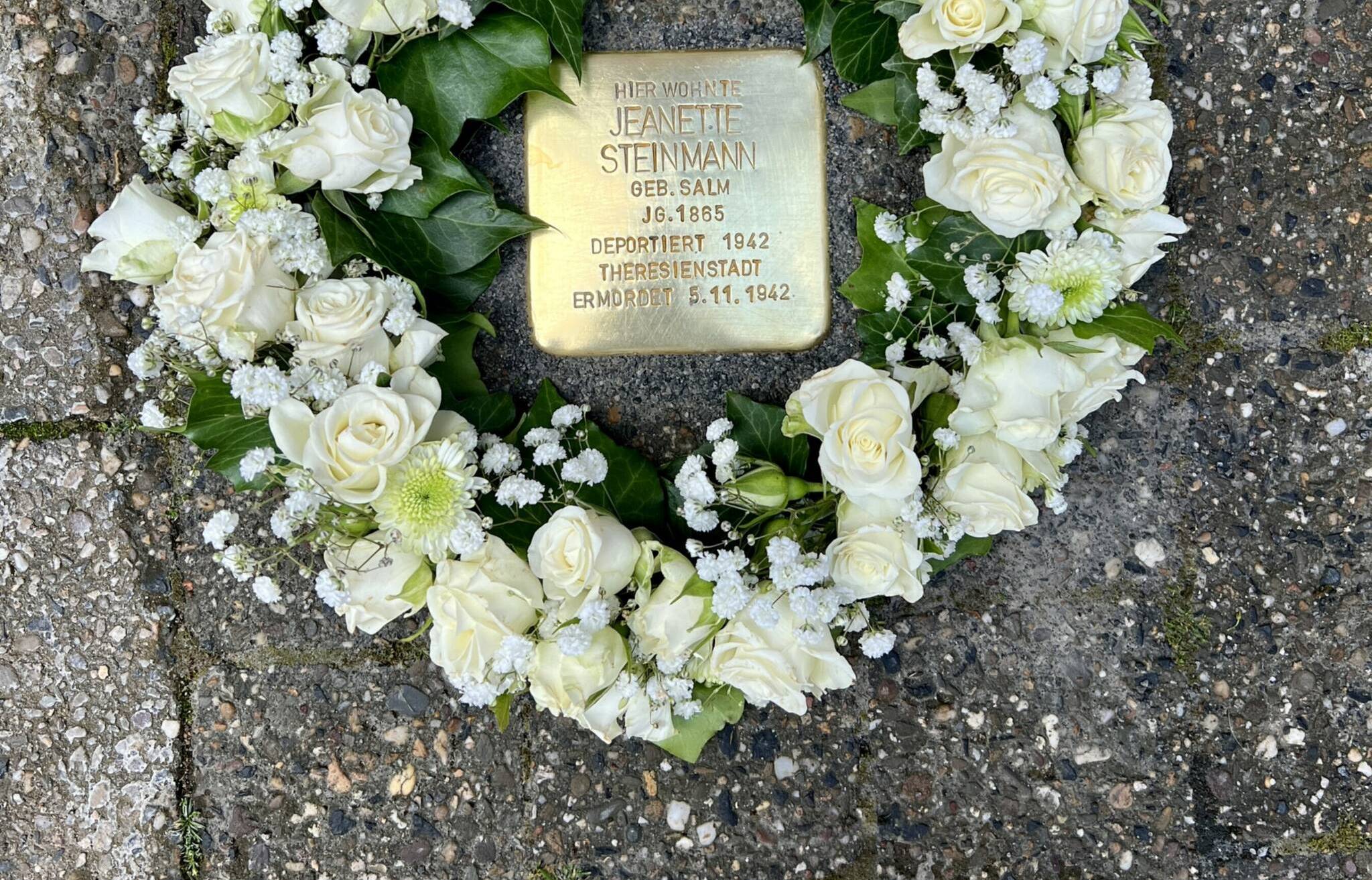 Der frisch verlegte Stolperstein wird von einem Rosenkranz geschmückt.