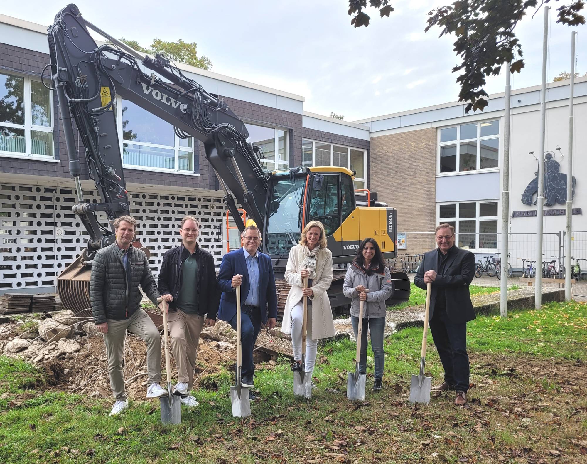 Frank Siegmeyer (OGS-Koordinator Schülergarten), Sebastian Posthaus (Fachdienstleiter Hochbau, Tiefbau, Bauhof), Sascha Solbach (Bürgermeister der Stadt Bedburg), Mirjam Herrwegen (Rektorin Martinusschule), Meltem Ayberk (stellvertretende Fachdienstleitung Hochbau, Tiefbau, Bauhof) und Heinz Berger (Berger Architekten) beim Spatenstich für die neue Mensa an der Martinusschule in Kaster.