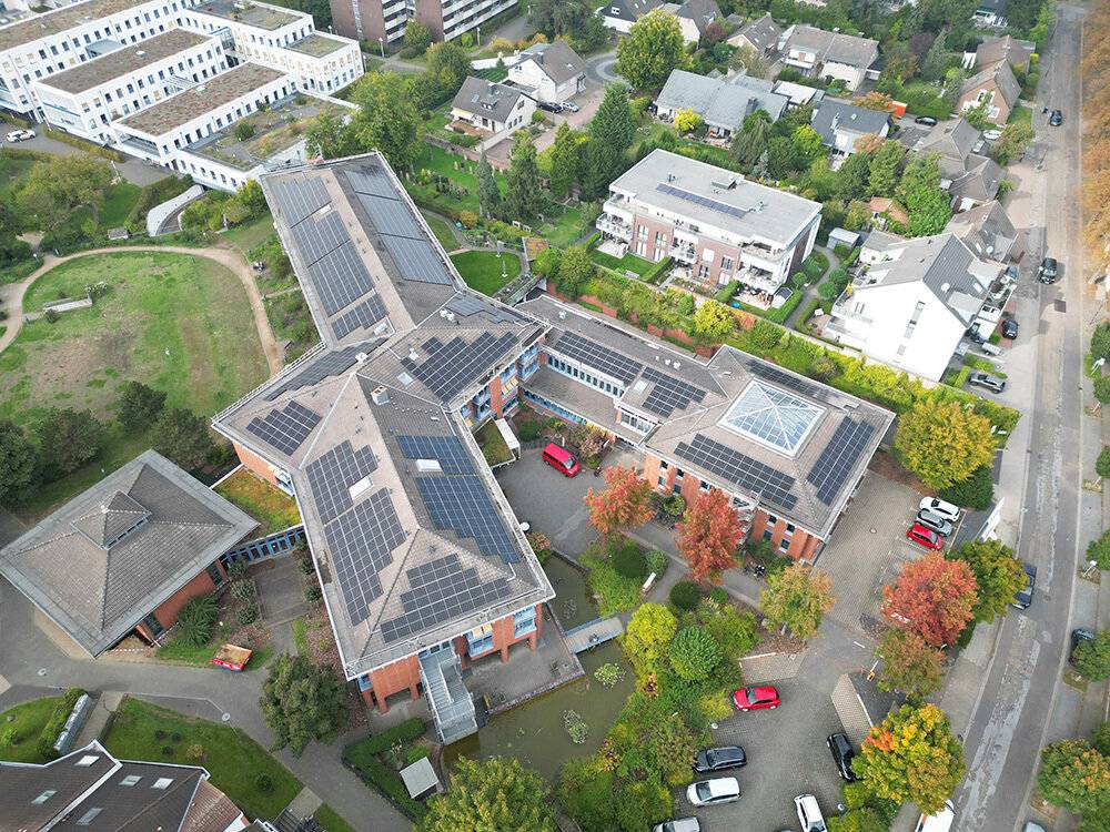 Aus der Vogelperspektive ist erkennbar, über welch große Dachanlagen die Caritas am Standort Grevenbroich verfügt und wie intensiv die Flächen nun mit Solar-Paneelen besetzt sind. Rechts die Montanusstraße, oben links die Ausläufer des „St. Elisabeth“-Krankenhauses mit dem Zentrum für Radiologie und Nuklearmedizin. Der sternenförmig verlaufende „St. Barbara“-Trakt – das „Haus der Familie“ – ist im Jahr 1997 zu seiner heutigen Architekturform erweitert worden.  Foto: Rheinland Solar
