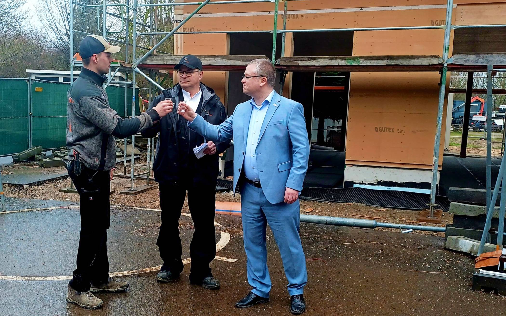  Von links: Hans-Günter Friedrichsen und Hauke van Elk vom Schreinerei- und Tischlerbetrieb „tischleraktiv“ stoßen mit Bürgermeister Philipp Sieben auf den Rohbau an.  